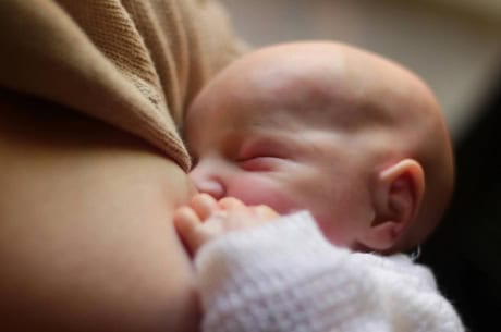 Baby breastfeeding after waking a newborn to feed
